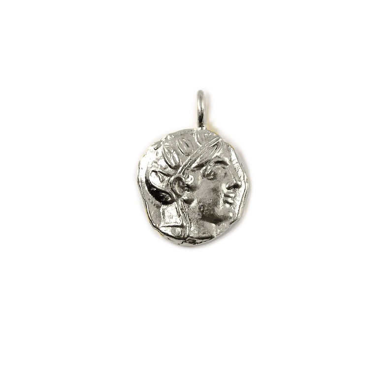 May include: Silver pendant featuring a detailed profile of a woman's face with a laurel wreath. The pendant has a slightly irregular, coin-like shape.
