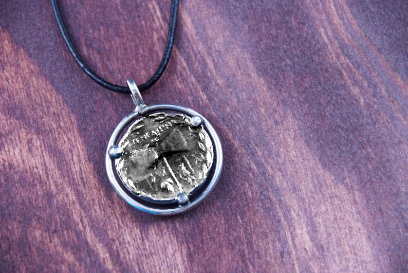 May include: A silver necklace with a round pendant featuring a gold coin with an inscription. The coin is set in a silver frame with four small silver beads.