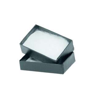 May include: An open, black rectangular gift box with a white, fluffy interior. The box is slightly ajar, revealing the soft, padded lining. The box is empty and ready for a small gift.