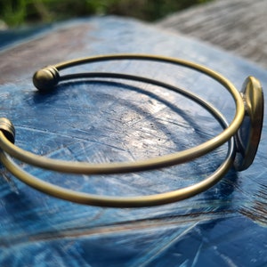 May include: A gold-toned bangle bracelet with a smooth, rounded finish. The bracelet is open and has a simple, elegant design.