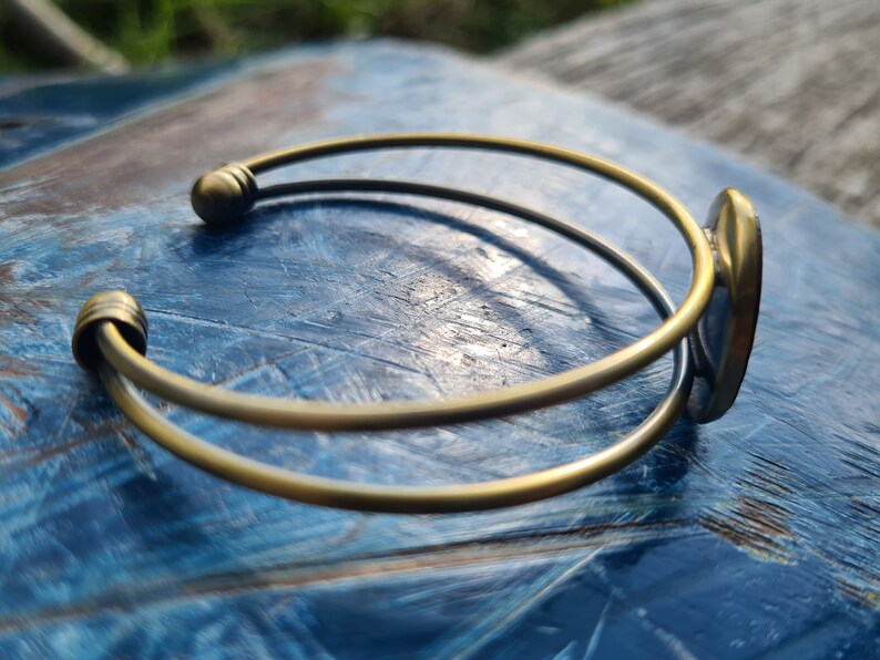May include: A gold-toned bangle bracelet with a smooth, rounded finish. The bracelet is open and has a simple, elegant design.