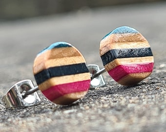 Könnte beinhalten: Ein Paar runde Holzohrringe mit einem mehrfarbigen Streifenmuster. Die Ohrringe sind aus recyceltem Skateboardholz gefertigt und haben ein Farbschema in den Farben Türkis, Schwarz, Braun und Pink.