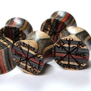 May include: Set of four wooden ear gauges with a compass design and runes carved into the wood. The gauges are made of different types of wood, including red, black, and brown.