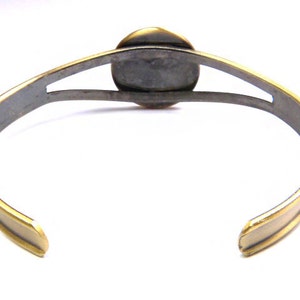 May include: A gold and silver bracelet with a round, open design in the center. The bracelet is made of metal and has a polished finish.