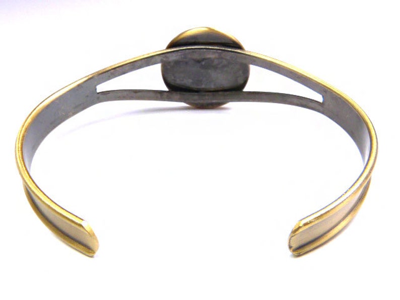 May include: A gold and silver bracelet with a round, open design in the center. The bracelet is made of metal and has a polished finish.