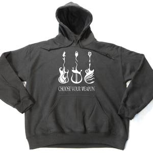 May include: Dark gray hoodie with a front pocket and a hood. The front of the hoodie features a white graphic of three stylized guitars with the text "CHOOSE YOUR WEAPON" below them. The hoodie is made of a soft, comfortable material.