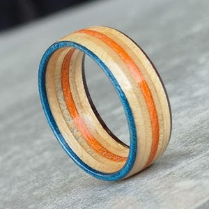 May include: A wooden ring with blue and orange stripes. The ring is made from recycled skateboard wood.