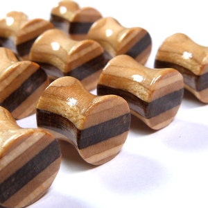May include: A set of wooden ear gauges with a natural wood grain and black stripes. The gauges are in various sizes and are arranged in a row.