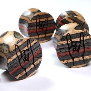May include: Set of four wooden ear gauges with a striped pattern and a rock and roll hand symbol design. The gauges are made of wood and have a natural finish.