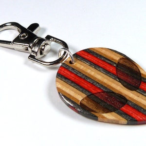 May include: A wooden keychain shaped like an alien head with red and black stripes. The keychain has a silver metal loop.