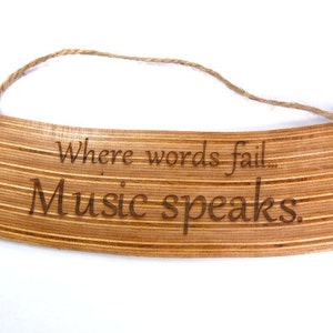 May include: Wooden sign with a rustic, natural finish. The sign is engraved with the text "Where words fail... Music speaks."