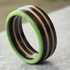 May include: A wooden ring with black and natural wood stripes and a green edge.