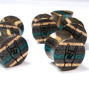 May include: A set of eight wooden ear gauges with a black, white, and blue striped pattern. Each gauge features a laser-etched rock and roll hand symbol.