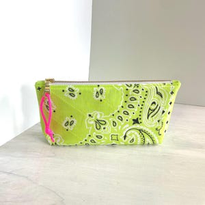 May include: A lime green zippered pouch with a black and white paisley pattern. The pouch has a gold zipper and a bright pink pull. The fabric is quilted with a diamond pattern.