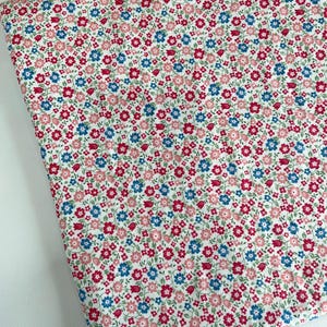May include: A folded piece of fabric featuring a dense, repeating pattern of small flowers in shades of pink, red, and blue on a white background. The floral design includes tiny blossoms and buds with green stems scattered across the surface.