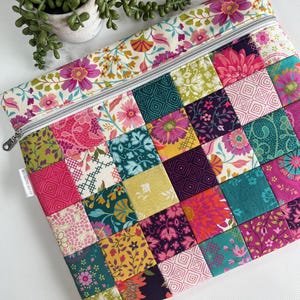 May include: A colorful patchwork zippered pouch featuring a variety of floral and geometric patterns in shades of pink, teal, yellow, and purple. The top edge has a floral print with a silver zipper. The pouch is likely made of fabric.