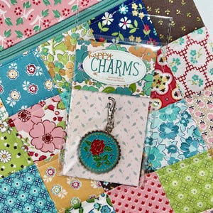 May include: A patchwork fabric background with a zippered pouch and a charm. The charm is teal with a red rose design and a silver-coloured clasp. The packaging reads "happy CHARMS".
