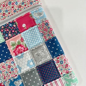 May include: A rectangular zipped pouch featuring a patchwork design of various cotton fabrics. The squares display patterns including floral prints in red, pink, and blue, white polka dots on navy, grey cat illustrations, and red and white stripes.