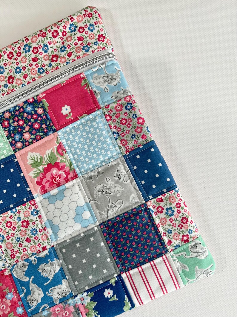 May include: A rectangular zipped pouch featuring a patchwork design of various cotton fabrics. The squares display patterns including floral prints in red, pink, and blue, white polka dots on navy, grey cat illustrations, and red and white stripes.