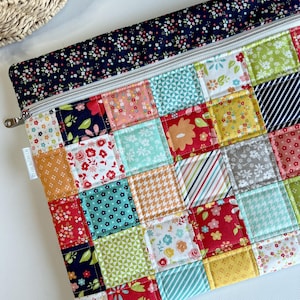 May include: A colorful patchwork zippered pouch with a navy floral top. The pouch features a variety of patterned squares in red, pink, yellow, green, and blue. The zipper is silver, and the pouch is likely handmade.