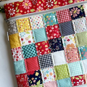 May include: A patchwork zippered pouch with a red floral top and a variety of patterned squares in shades of red, yellow, blue, and green. The pouch has a silver zipper and is quilted.