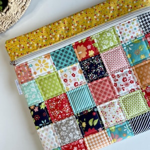 May include: A quilted patchwork zipper pouch featuring a vibrant mix of floral and geometric patterns in red, green, blue, and yellow. The top edge is a solid yellow with small floral accents. The pouch has a silver zipper and a small tag that reads "OLD BASS BERRY CO."