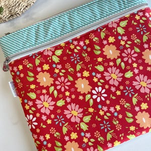 May include: A red zippered pouch with a floral pattern featuring pink, orange, yellow, and white flowers. The top edge has a light blue and white striped fabric. The zipper is silver.