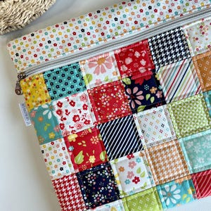 May include: A colorful patchwork zippered pouch with a variety of floral, striped, and patterned fabric squares. The pouch has a white zipper and a floral patterned border. The label says "Red Raspberry Co."
