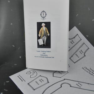 May include: A white booklet titled Louis Clothing Pattern and Instructions for a 1:12 Scale Dollhouse Doll, featuring a photo of a doll in a gold coat. Below it, a paper sheet shows black line drawings of pattern pieces with a one-inch scale bar.