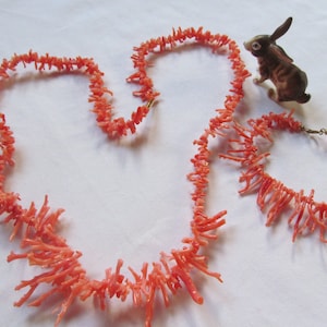 May include: A set of two coral necklaces, one long and one shorter, made of bright pink coral branches. The necklaces are displayed on a white surface.