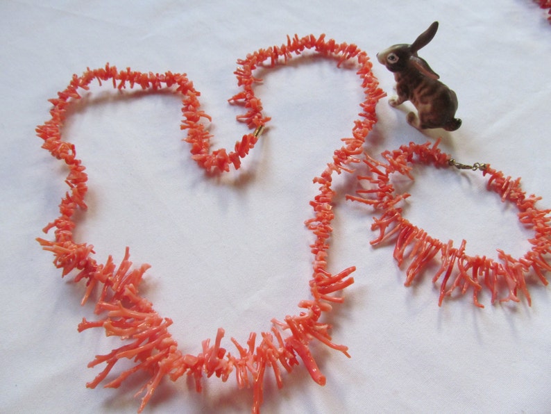 May include: A set of two coral necklaces, one long and one shorter, made of bright pink coral branches. The necklaces are displayed on a white surface.