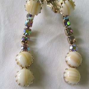 May include: A pair of gold tone clip-on earrings with iridescent rhinestones and white shell-like beads.