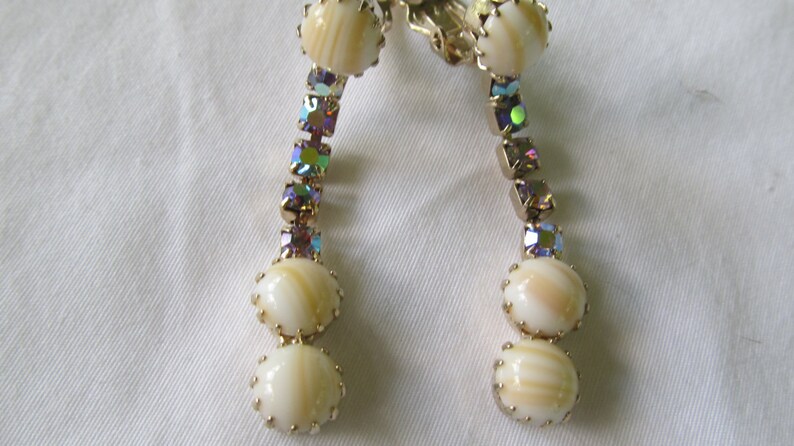 May include: A pair of gold tone clip-on earrings with iridescent rhinestones and white shell-like beads.