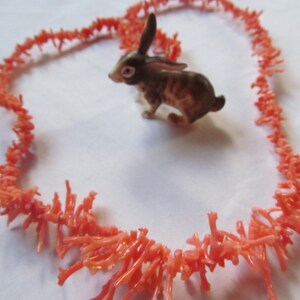 May include: A coral necklace made of small, delicate branches of coral. The coral is a vibrant orange color and is arranged in a loose, flowing pattern. The necklace is laid out in the shape of a heart.
