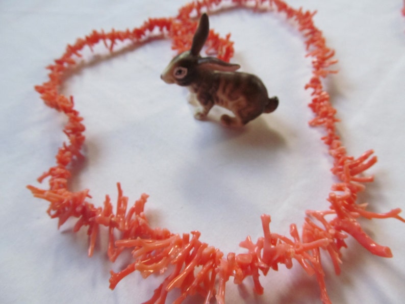 May include: A coral necklace made of small, delicate branches of coral. The coral is a vibrant orange color and is arranged in a loose, flowing pattern. The necklace is laid out in the shape of a heart.