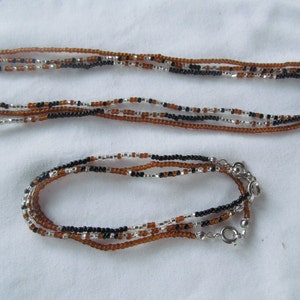 Puede incluir: Un conjunto de dos collares hechos de cuentas marrones, negras y plateadas. El collar m&aacute;s largo mide aproximadamente 40 pulgadas y el collar m&aacute;s corto aproximadamente 18 pulgadas. Ambos collares tienen un cierre plateado.