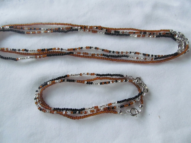 Puede incluir: Un conjunto de dos collares hechos de cuentas marrones, negras y plateadas. El collar m&aacute;s largo mide aproximadamente 40 pulgadas y el collar m&aacute;s corto aproximadamente 18 pulgadas. Ambos collares tienen un cierre plateado.
