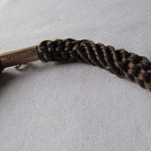 May include: A brown braided hair bracelet with a gold clasp. The clasp has the inscription "14K GF" on it.