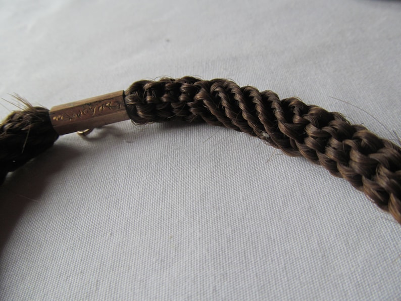 May include: A brown braided hair bracelet with a gold clasp. The clasp has the inscription "14K GF" on it.