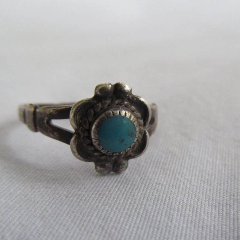 May include: A silver ring with a turquoise stone set in a floral design.