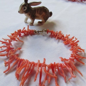 May include: A coral necklace made of small, delicate branches of coral. The necklace is pink in color and has a gold clasp.