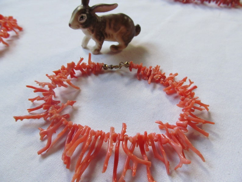 May include: A coral necklace made of small, delicate branches of coral. The necklace is pink in color and has a gold clasp.