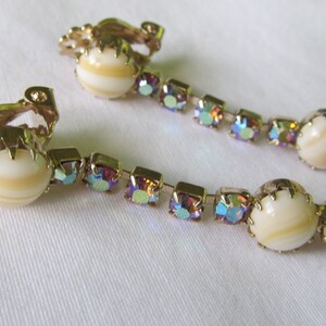 May include: A pair of gold tone clip-on earrings with iridescent rhinestones and white shell-like cabochons.