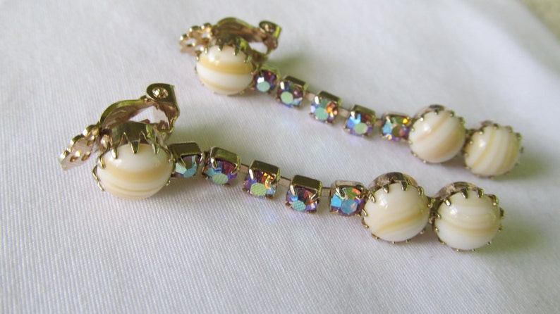 May include: A pair of gold tone clip-on earrings with iridescent rhinestones and white shell-like cabochons.