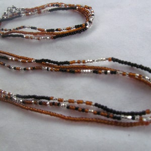 Puede incluir: Un conjunto de collar y pulsera de m&uacute;ltiples hilos hecho con cuentas marrones, negras y plateadas.