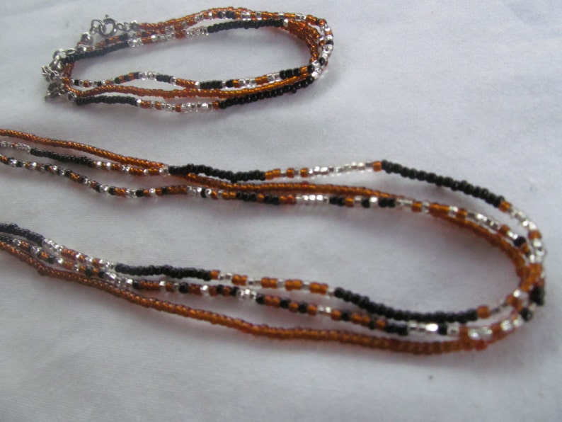 Puede incluir: Un conjunto de collar y pulsera de m&uacute;ltiples hilos hecho con cuentas marrones, negras y plateadas.