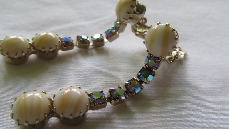 May include: A pair of clip-on earrings with iridescent rhinestones and white shell-like cabochons.
