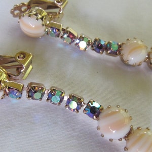May include: A pair of gold tone clip-on earrings with iridescent rhinestones and white shell-like beads.