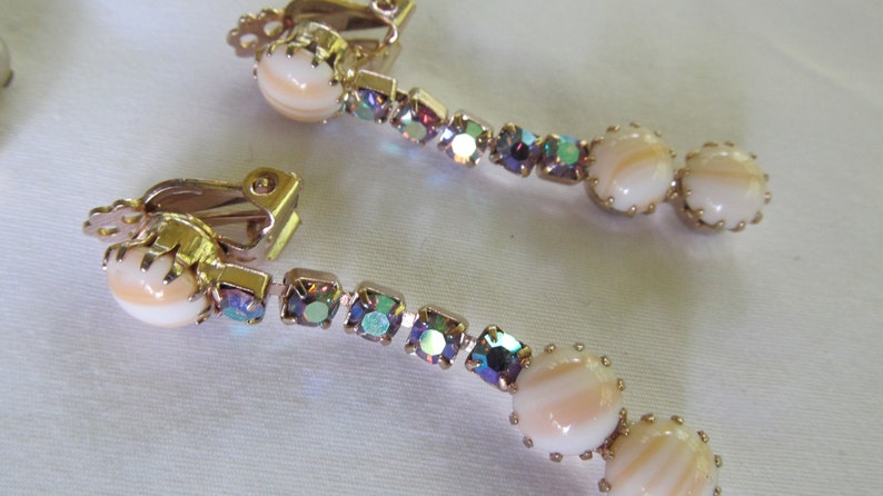 May include: A pair of gold tone clip-on earrings with iridescent rhinestones and white shell-like beads.