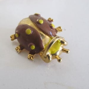 May include: A gold-tone ladybug brooch with brown and yellow enamel. The ladybug has yellow spots and a yellow underbelly.
